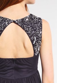 Navy dress with an open back, embellished neckline featuring intricate beadwork, and textured fabric. Zipper detail at the lower back.