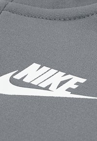 Grauer Sweatshirtstoff mit einem auffälligen weißen Nike-Logo mit einem Swoosh, Texturdetails sichtbar im Gewebe des Materials.