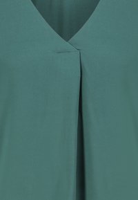 Teal fabric with a V-neckline and central inverted pleat detail on a garment.