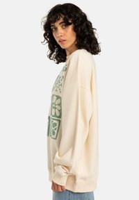 Crème sweatshirt met groene bloemenpatronen, oversized pasvorm, ribgebreide manchetten en hoge kraag. Glad textuur en zacht materiaal.