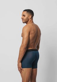 Boxershorts aus dunkelblauem Stoff mit einem schwarzen elastischen Bund. Glatte Textur, mittellange Schnittform, eng am Körper anliegend.