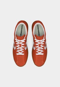 Ζευγάρι κόκκινων παπουτσιών Converse με λευκά κορδόνια και λογότυπο αστεριού σε σχήμα κεραυνό, σε θέαση από πάνω σε λευκό φόντο.