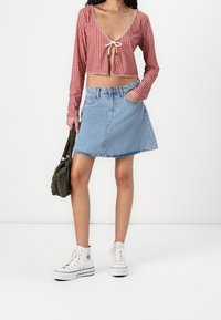 Karmesinrot karierter Langarm-Crop-Top mit V-Ausschnitt und Bindungsdetail, kombiniert mit einem hellblauen Denim A-Linien-Rock und weißen High-Top-Sneakern.