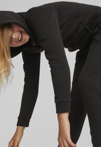 Felpa nera con zip e pantaloni jogger coordinati realizzati in tessuto morbido. Presenta una tasca frontale, polsini e una vestibilità comoda.