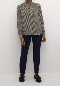 Langsleeve blouse met een hoge kraag, met een zwart en crèmekleurig ruitpatroon. Gecombineerd met donkerblauwe rechtaflopende jeans en zwarte loafers.