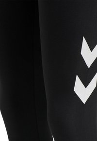 Leggings de sport noirs avec une texture lisse, ornés d'un motif en chevron blanc sur le côté pour un détail supplémentaire.