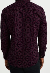 Hedvábná košile s dlouhým rukávem v tmavě fialové barvě, zdobená geometrickým černým vzorem. Obsahuje límec na knoflíky a detaily zakřiveného spodního lemu.