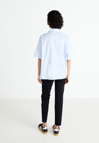 Light blue short-sleeve shirt with a straight cut, worn with black slim-fit pants and black and white sneakers. Flat texture, no patterns.