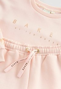 Jasnoróżowa bluza z złotym napisem "BAKER by TED BAKER". Zawiera elastyczny pas oraz sznurki ze złotymi akcentami i markowym logo.