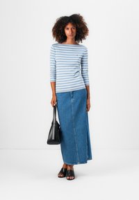 Stripete blå og hvite langermede skjorte med rund hals, parret med et langt denimskjørt, svart håndveske og svarte sandaletter.