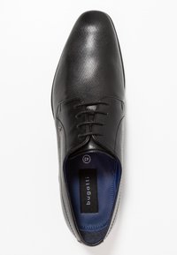Zapato de vestir de cuero negro con una superficie texturizada, punta redondeada y diseño con cordones. Presenta un interior azul y una etiqueta de la marca visible.