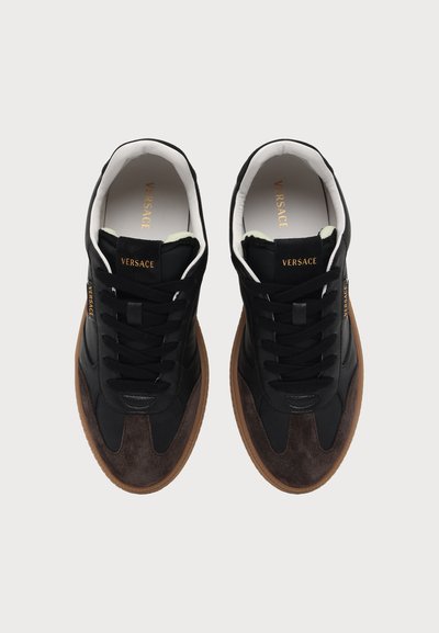 Paire de baskets Versace noires et marron avec intérieur blanc, lacets noirs et marquage Versace doré sur la languette et le côté.