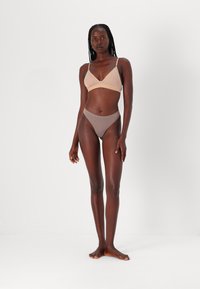 Bralette triangle beige avec bretelles réglables et ceinture marron clair. Culottes taille haute beiges en tissu doux avec une texture lisse.