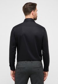 Zwart shirt met lange mouwen, een gladde textuur, gestructureerde kraag en manchetten met knopen, gecombineerd met grijze broek met patroon.