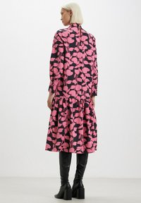 Abito a maniche lunghe in tessuto nero con motivo floreale rosa. Presenta un orlo a strati e una chiusura a oblò sul retro. Indossato con stivali neri al ginocchio.