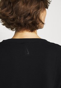 Schwarzes, gestricktes Sportshirt mit rundem Ausschnitt und einem dezenten Nike-Logo auf der Rückseite. Strukturierter Stoff sorgt für visuelle Abwechslung.