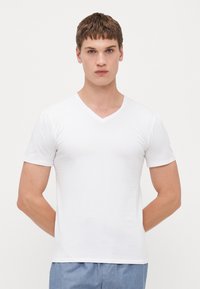 T-shirt blanc à manches courtes en V fabriqué à partir d'un tissu doux, affichant une coupe ajustée et une texture lisse, sans motifs ni accents.