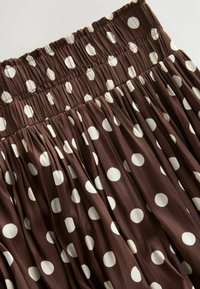 Gonna a pois marrone con vita arricciata. Presenta pois bianchi cremosi di varie dimensioni su un tessuto fluente e testurizzato.