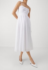 Vit midi-klänning med spaghettistänger, struktur tyg, samlad byst och utsvängd kjol. Matchas med vita spetsiga klackar.