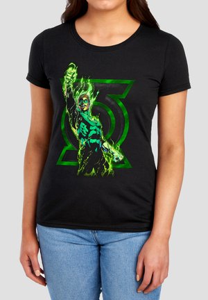 Frau, die ein schwarzes T-Shirt mit einem leuchtend grünen Superhelden trägt, der eine Faust hebt, und einem Green Lantern-Symbol im Hintergrund.