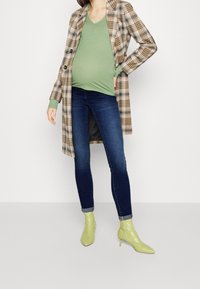 Rutiga långkappa, grön ribbad topp, mörka slim fit jeans, ljusgröna ankelstövlar. Har v-ringning, knappar och figursydd siluett.