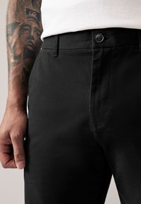 Pantalones negros de tela suave, con cierre de botón en la cintura y un ajuste entallado con detalles mínimos de costura.