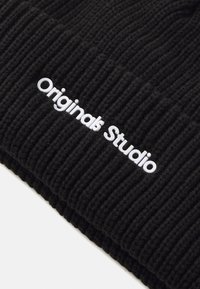 Zwarte geribbelde beanie van gebreide stof, met een op de voorkant geborduurd wit "Originals Studio" logo.
