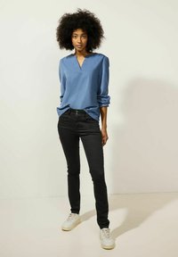 Blusa de manga larga azul clara con escote en V, combinada con jeans ajustados negros y zapatillas blancas. Tejido suave con un ligero brillo.