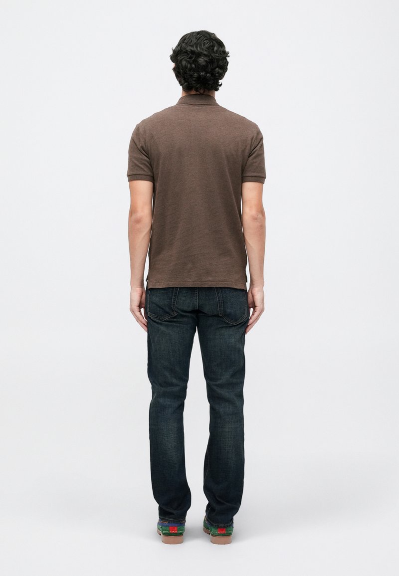 Braunes Polo-Shirt mit kurzen Ärmeln, kombiniert mit dunklen Jeans. Das Shirt verfügt über einen Kragen und ein gerades Design.