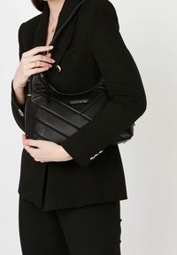 Sort skuldertaske i læder med quiltet mønster, udstyret med gulddetaljer, en buet top og en tynd rem. Logo vist på forsiden.