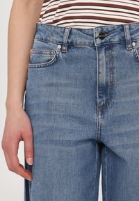 Light blue denim jeans with a high waist, five-pocket design, and subtle stitching details. Features a metal button closure and zipper.