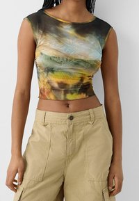 Kort topp i lätt, genomskinligt tyg med abstrakta mönster i grönt, brunt och gult; åtsittande design med rund halsringning.
