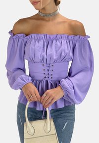 Lavendel Off-Shoulder-Bluse mit voluminösen Ärmeln, tailliert mit silbernen Ösen, kombiniert mit einer beigen Handtasche im Krokodillederdesign.