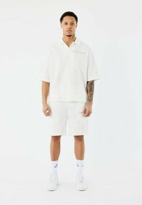 Witte, gestructureerde, kortegeselecteerde shirt en bijpassende shorts, voorzien van subtiele cactuspatronen en geborduurde details, gecombineerd met witte sneakers.