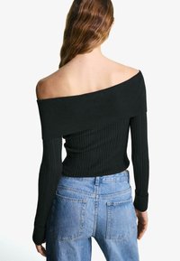 Black ribbed off-the-shoulder top with long sleeves, paired with high-waisted light blue denim jeans, showcasing a fitted design.