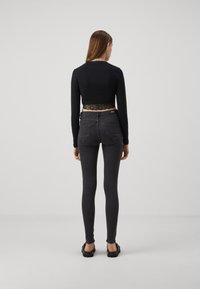 Svart avkortet topp med blondekant, kombinert med mørk grå skinny jeans. Modell sett bakfra, iført svarte flate sko. Enkelt, tettsittende design.