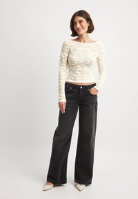 Långärmad, krämfärgad topp med ett strukturerat, randigt mönster. Kombinerad med högmidjade, vida svarta jeans och beiga skor med spetsig tå.