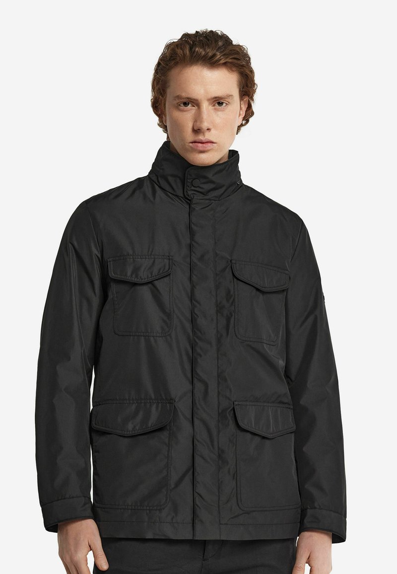 Svart vattentät jacka med hög krage, två bröstfickor och en slät yta. Utformad med knappaccenter och dragkedjefront.