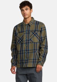 Camicia in flanella a quadri verdi e blu navy con chiusura a bottoni, due tasche sul petto e bottoni in plastica. Tessuto morbido e vestibilità casual.