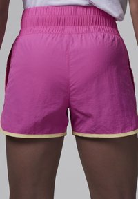 Pantaloni corti rosa con cintura elastica, rifiniture gialle e tasche laterali. Il materiale sembra leggero e spiegazzato.