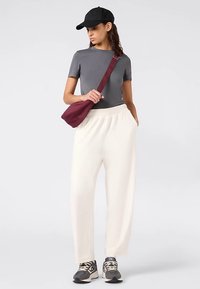 Grijs aansluitend T-shirt, losse witte sweatpants, zwarte pet, bordeauxrode crossbodytas en grijze sneakers met zwarte accenten. Zachte stoftexturen.