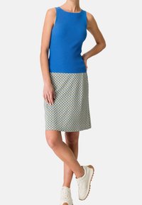 Débardeur bleu côtelé associé à une jupe imprimée jusqu'aux genoux avec un motif géométrique. Des baskets blanches complètent la tenue.