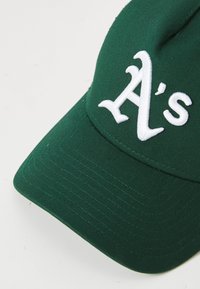 Vihreä pesäpallohattu, jossa on valkoisella brodeerattu "A's" -logo etupaneelissa, valkoista taustaa vasten.