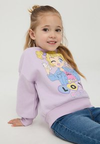 Felpa viola con stampa grafica che presenta una ragazza dei cartoni animati che tiene un telefono. Polsini e orlo a costine. Abbinata a jeans blu.