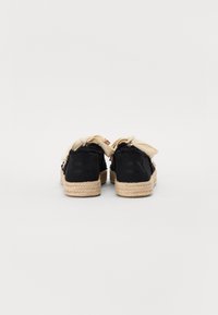 Scarpe di stoffa nere con suola in corda di paglia, dotate di un accento di fiocco crema e retro testurizzato, che mostrano un design espadrille casual.
