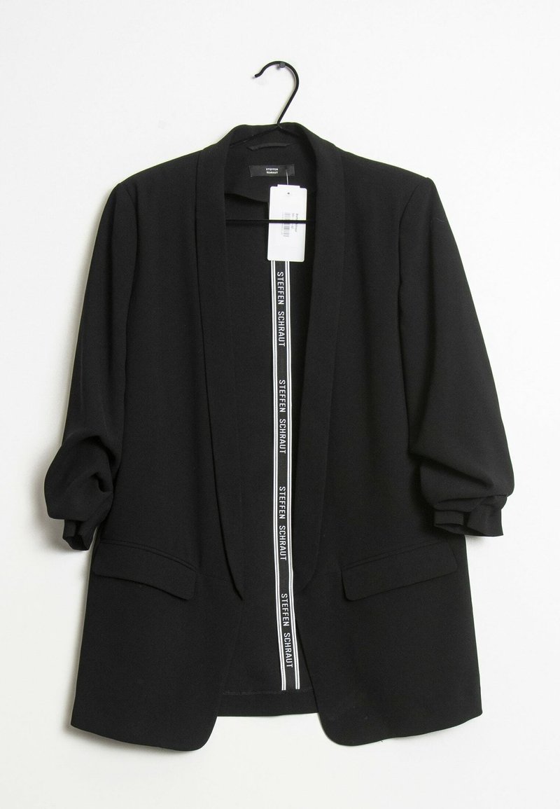 Blazer noir à ouverture avant avec manches froncées et poches à rabat, suspendu sur un cintre noir contre un fond blanc.