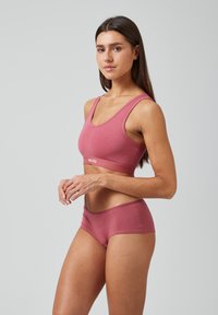Completo a due pezzi in rosa tenue. Il reggiseno presenta uno scollo a barchetta e spalline larghe, mentre le culotte hanno una silhouette morbida con una vita a banda.