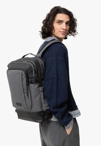 Zaino a quadri nero e grigio con una texture liscia, spallacci imbottiti, molteplici scomparti e fondo rinforzato.