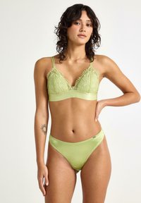 Vihreä pitsinen bralette, jossa on satiinihihna ja säädettävät hihnat, yhdistettynä vastaaviin satiinisiin bikineihin, joissa on aaltoilevat reunat.