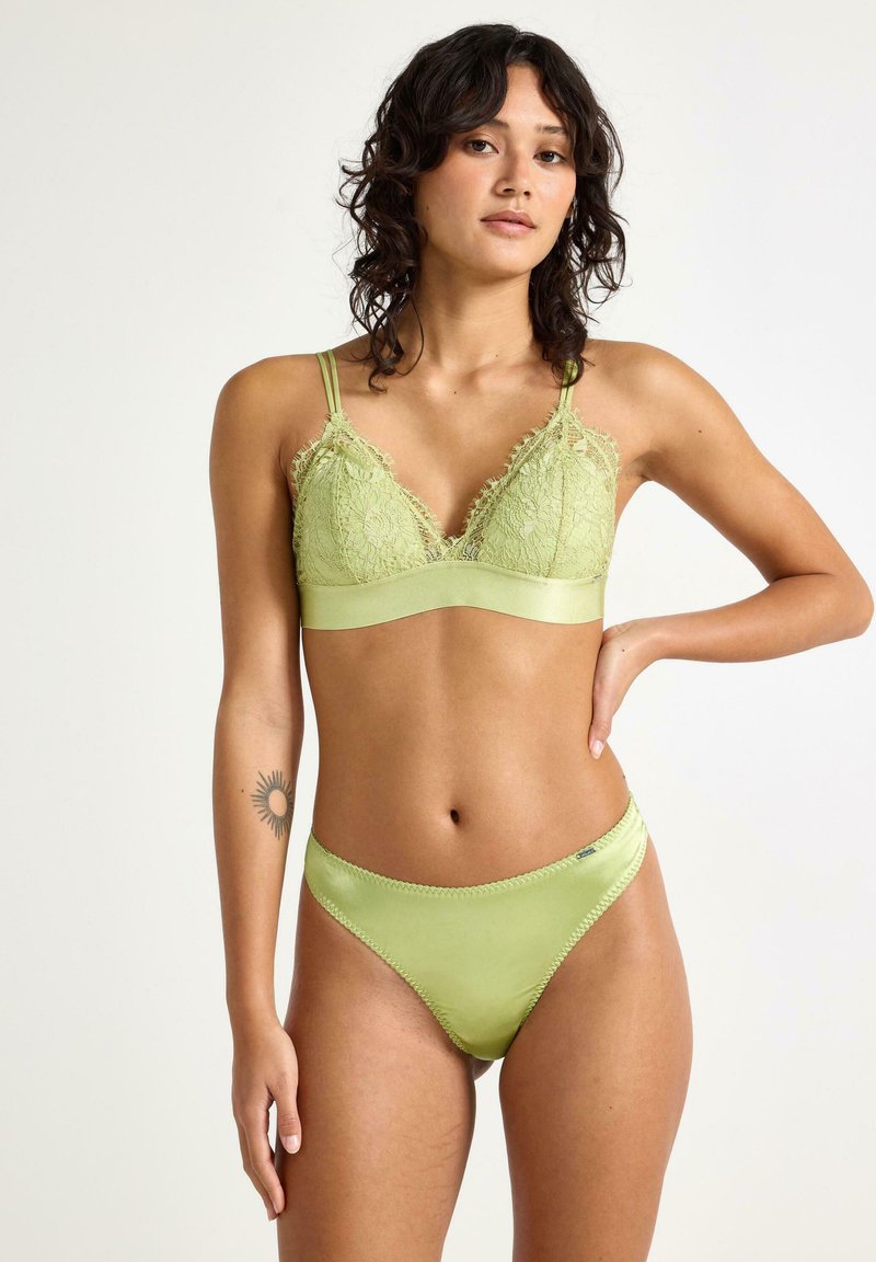 Vihreä pitsinen bralette, jossa on satiinihihna ja säädettävät hihnat, yhdistettynä vastaaviin satiinisiin bikineihin, joissa on aaltoilevat reunat.